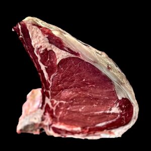 Bistecca alla fiorentina taglio costola su fondo nero, in piedi sull&rsquo;osso: l&rsquo;occhio di carne e il bordo di grasso