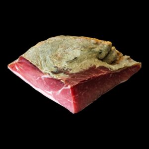 Trancio di prosciutto crudo su fondo nero: la parte magra rossa, il grasso bianco e la crosta di sugna in superficie